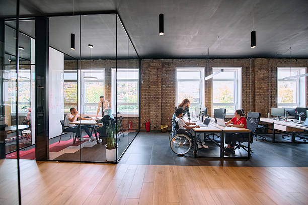 A diverse group of business professionals collaborates in a modern startup coworking center, utilizing a mix of paper-based and technological tools such as mobile phones and computers stock photo