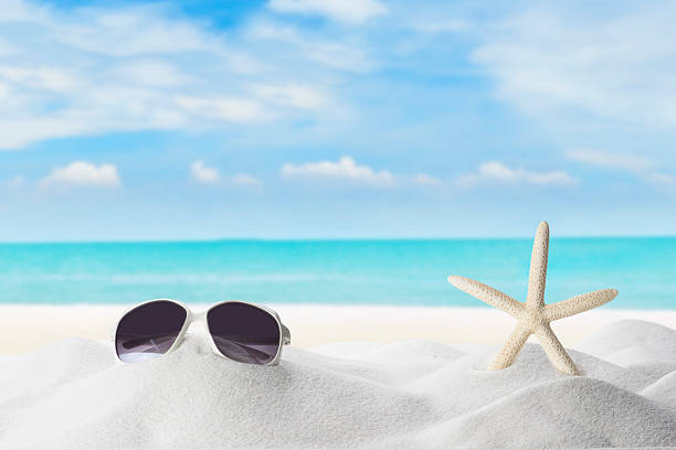 Sunglass and Star Fish  On White Sand Beach with Ocean Wave Splashing with Cloudy Blue Sky