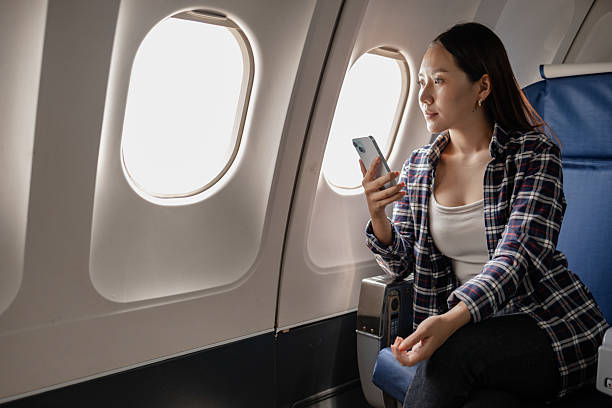 istock Asian woman smiling while using her smartphone on an airplane. She is sitting next to the window, enjoying her time during the flight. The atmosphere appears relaxed and comfortable. 2238451339