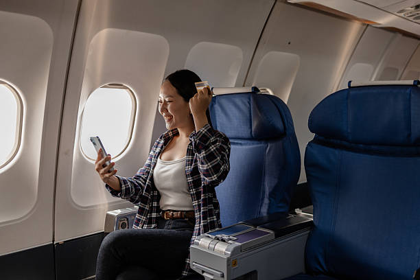 istock Smiling Asian woman celebrating while holding a credit card and using smartphone on an airplane, showing excitement after a successful online payment or shopping during her flight. 2238451398