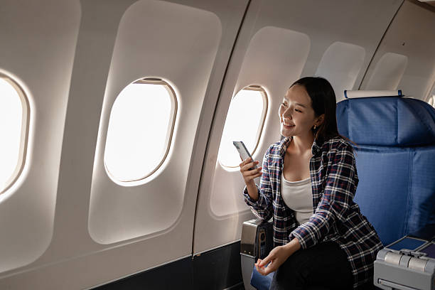 istock Asian woman smiling while using her smartphone on an airplane. She is sitting next to the window, enjoying her time during the flight. The atmosphere appears relaxed and comfortable. 2238451412