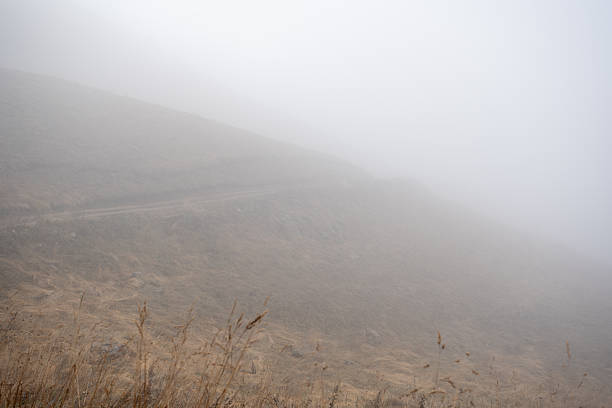 Winding mountain road disappearing into thick fog and mist