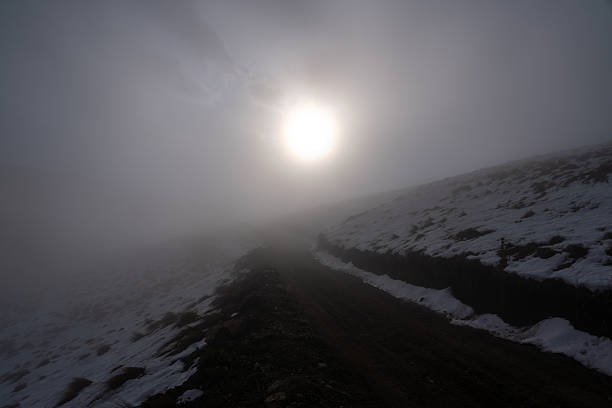 Lonely mountain path in thick fog with snow and glowing winter sun