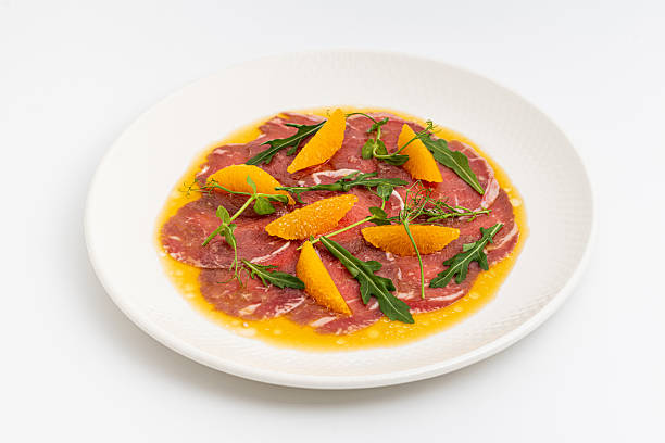 Thinly sliced beef carpaccio with orange segments and arugula leaves