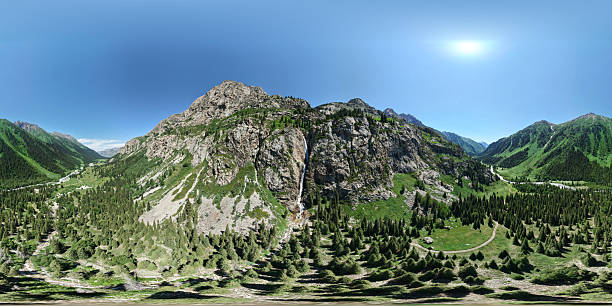Breathtaking panoramic view of a waterfall cascading down a rocky mountainside into a lush green valley with coniferous forests under a clear blue sky Burkhan Bulak National Park, Kazakhstan