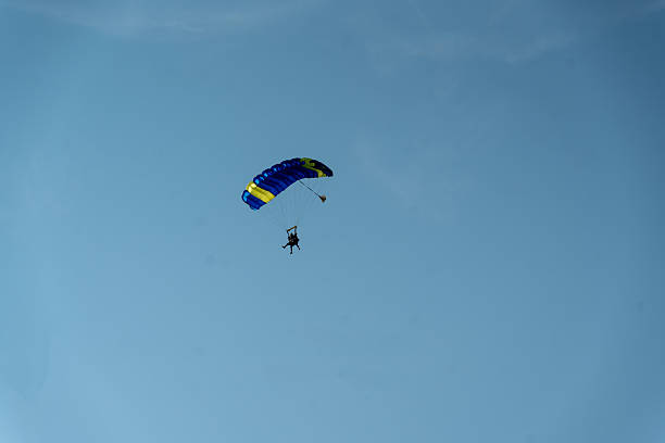 A parachutist under a vibrant canopy prepares for a controlled landing in an open sky. The ascent and descent highlight adrenaline and precision, with an airfield and distant landscape providing a calm backdrop. Ideal for sports, adventure, and outdoor recreation collections.