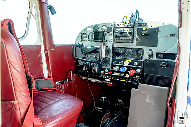 Inside a small aircraft cockpit, red leather seats frame a busy instrument panel filled with gauges, switches, and radios. Headphones rest at hand, wires neatly arranged as the pilot prepares for takeoff. This intimate view captures precision, focus, and the calm priority of safe, controlled flight.