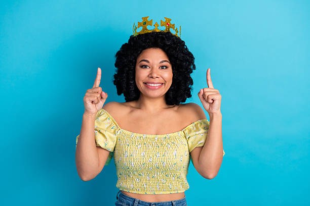 istock Joyful woman wearing crown gesturing upward with both hands against vibrant blue background 2238489874