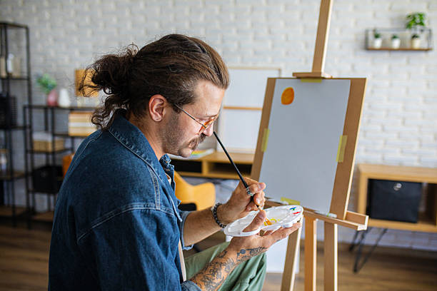 istock Creative man painting artwork on canvas in a modern apartment filled with natural light 2238496811