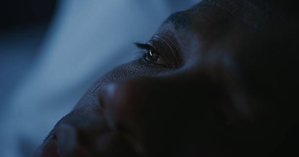 Close up African American Man Lying in Bed at Night, Scrolling Through Social Media. Image From Smartphone Reflected in Pupils. Concept Poor Sleep, Digital Habits, Poor Quality Rest. Static Shot.