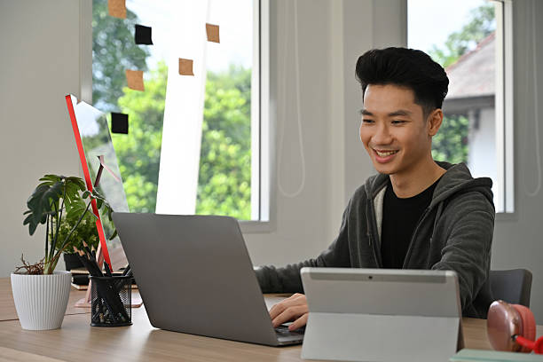istock Happy Young Asian male graphic designer focusing on digital projects with multiple devices 2238499706