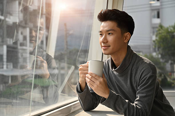 istock A young man enjoying a warm drink by the window, reflecting peacefully while holding a white mug in natural sunlight 2238500346