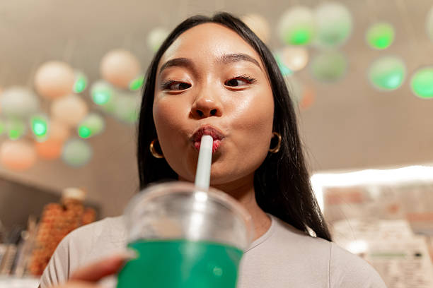 A close up fun shot of a young woman savouring a vibrant blue bubble tea in a cozy shop in Newcastle, in the north east of England. The playful lighting and colourful decor create a fun, modern atmosphere as she enjoys her drink, capturing the cheerful and trendy vibe of the city’s growing bubble tea scene.Videos are available similar to this scenario.