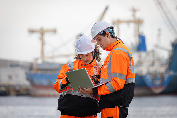 istock Port Engineers Teamwork and Technology at Shipping Terminal, Safety Uniformed Workers Using Laptop for Modern Logistics, Maritime Experts Planning Operations with Walkie Talkie on Dock 2238504142