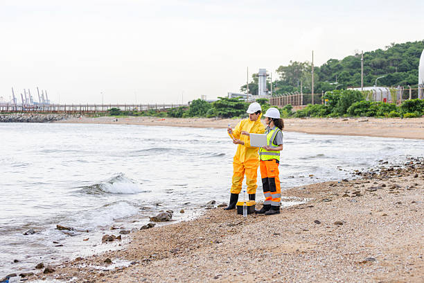 istock Environmental Engineers Testing Seawater Quality at Coast, Safety Officers Inspecting Coastal Area Near Industrial Port, Two Scientists in Safety Gear Analyzing Data on Beach 2238508053