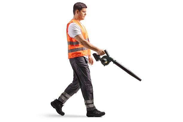 Full length profile shot of a municipal worker walking and using a leaf blower isolated on white background