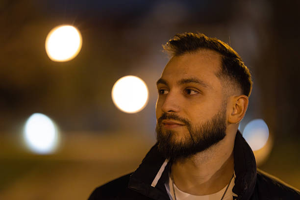 Young man standing outdoors at night with blurry background lights