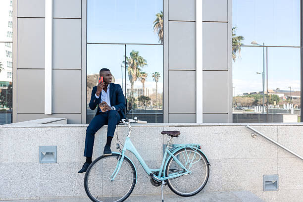istock Young businessman drinking coffee and talking by phone while sitting on wall near his bicycle 2238512935