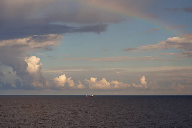 A beautiful view of a colorful rainbow arches over a peaceful ocean, with soft clouds drifting in the sky