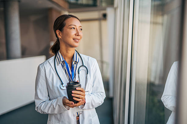 Asian doctor taking coffee break in hospital looking outside