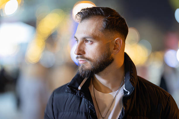 Young man standing outdoors at night, his profile facing away with blurred city lights behind