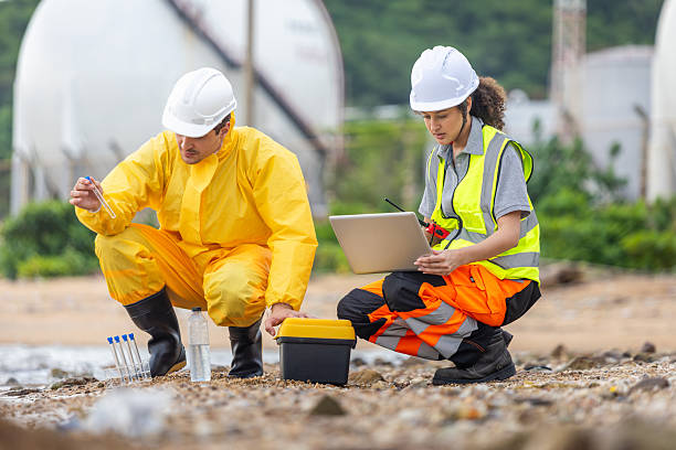 istock Environmental Engineers Testing Water Near Storage Tanks, Scientists in Protective Suits Collecting Liquid Samples for Analysis, Industrial Site Safety Team Conducting Environmental Field Survey 2238527006