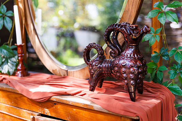 The image showcases a beautifully crafted horse-shaped ceramic jug resting on a wooden table. Surrounding it are lush plants and soft fabrics, creating a warm and inviting ambiance.