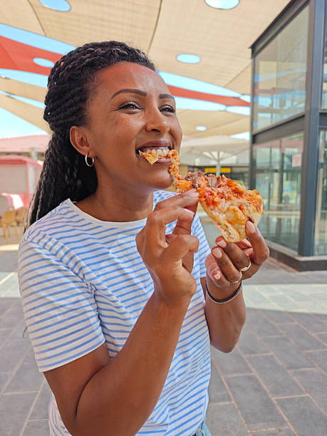 Joyful Woman Taking a Bite of Pizza Outdoors.