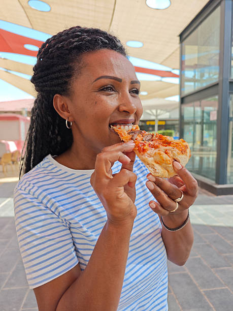 Smiling Woman Eating a Slice of Pizza Outdoors.