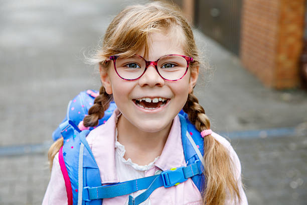 istock Happy little elementary school girl with eyeglasses and satchel backpack walking outdoors on the way to school. Smiling pupil child ready for back to school, education and childhood lifestyle concept. 2238548866