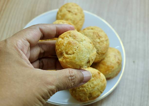 Hand picks up a golden round scone or biscuit from a plate. The freshly-baked surface is crispy, delicious, and ready-to-eat. Homemade snack concept.