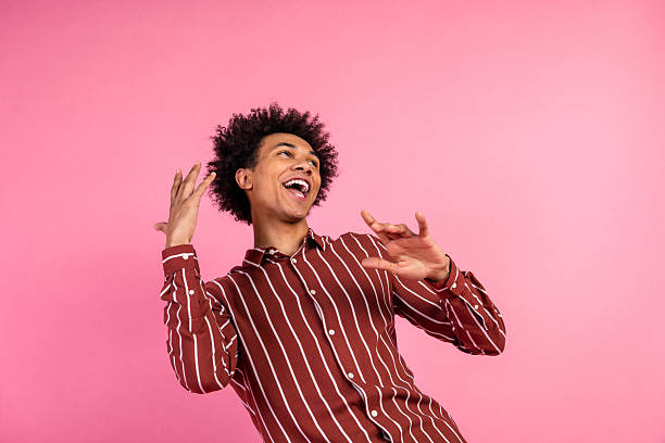 istock Cheerful young man in striped shirt poses with joyful expression against a bright pink background, showing energy 2238554292