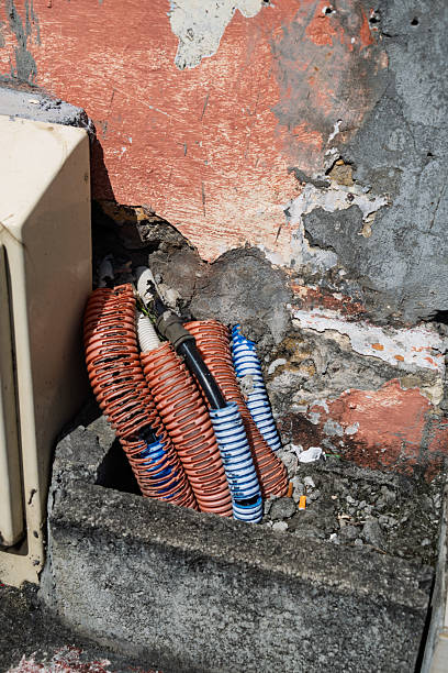 istock Air conditioning unit with coiled orange and blue hoses against weathered red brick wall in urban outdoor setting 2238559228