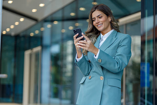 istock Businesswoman using smartphone outside modern office, smiling while checking messages or social media 2238559397