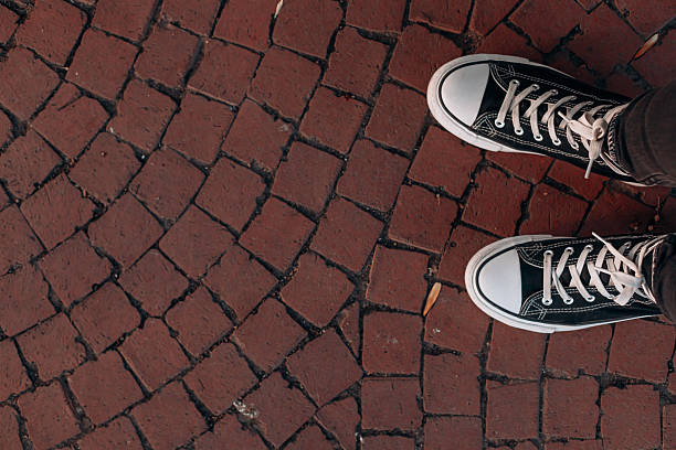 istock Black sneakers with white laces on red textured cobblestone pavement with visible cracks and natural patterns. 2238565083