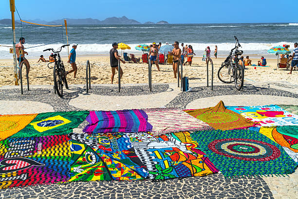 Vibrant beach scene in Rio de Janeiro featuring patterned blankets, sunbathers, cyclists, and a lively shoreline. Bright colors, urban seaside mood, and family-friendly summer fun by the sea.