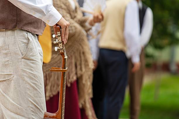 An elegantly dressed person holding a guitar near strolling couples in a park
