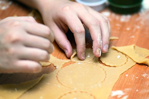 Child's hand picking up a piece of raw honey cookie dough for baking.