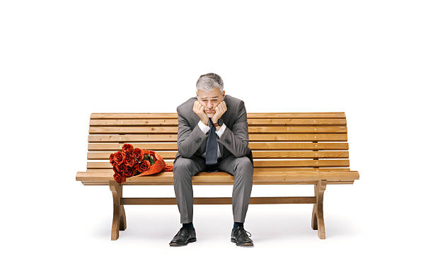 Photo of a handsome, bearded, male entrepreneur in a cream suit, having sunglasses on, sitting on a smart bench with a coffee in his hands. Facing up with his eyes closed, enjoying the quite moment