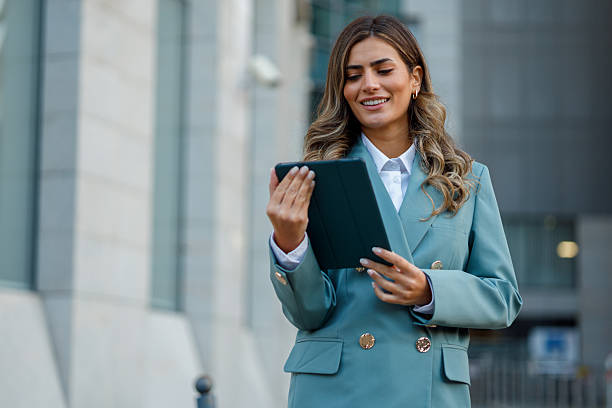 istock Young professional woman in blazer smiling while using a tablet outdoors in the city, working remotely and staying connected digitally 2238570356