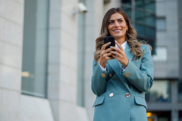 istock Young adult businesswoman smiling, using a smartphone for communication and technology while walking in a modern urban environment 2238571219
