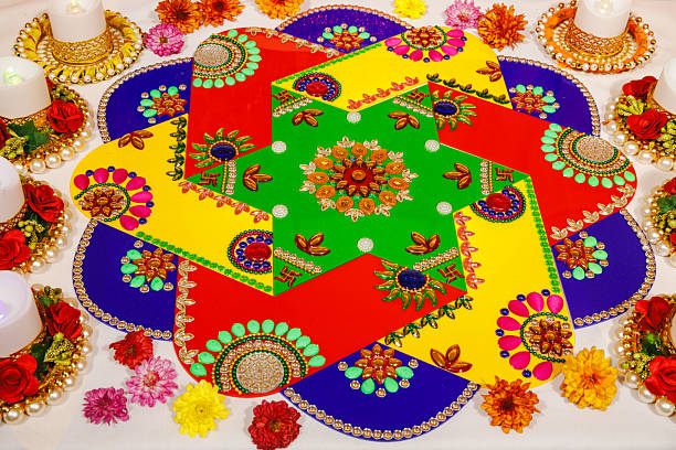 A close-up shot of a colorful flower rangoli, intricately designed with vibrant petals in shades of yellow, orange, and white. The delicate arrangement showcases traditional patterns and geometric shapes. The colors and natural textures bring a festive and welcoming ambiance, perfectly embodying the spirit of celebration for occasions like Diwali.