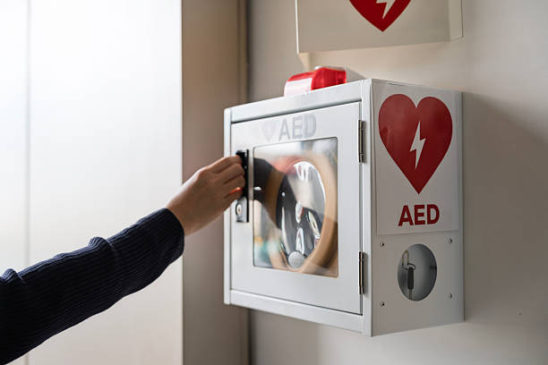 Close-up of a person’s hand opening an AED defibrillator box on the wall, highlighting emergency preparedness, healthcare safety, and lifesaving equipment in public spaces.