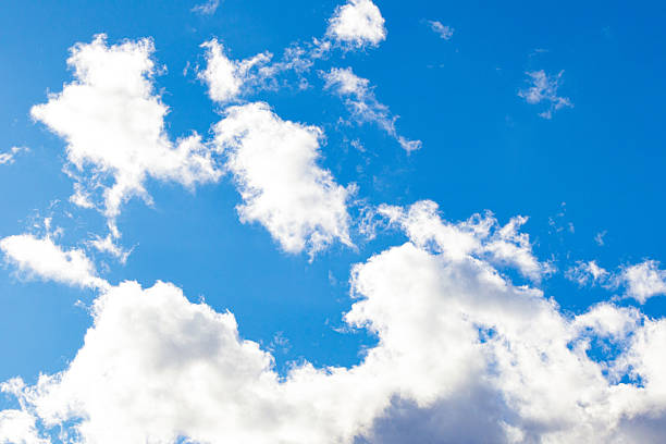 Bright blue sky with fluffy white clouds. Natural background with soft cloud shapes illuminated by sunlight. Perfect for weather, nature, and landscape themes.