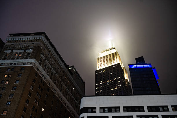 March 17, 2025: New York City, United States: On a foggy spring night the light of the Empire State Buildings casts a glow around the top of the skyscraper.