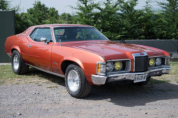 Osona, Spain – June 14, 2025: A front view of a classic Mercury Cougar XR7 from 1971-1973, highlighting its orange-red paint, yellow headlights, and a shiny chrome bumper