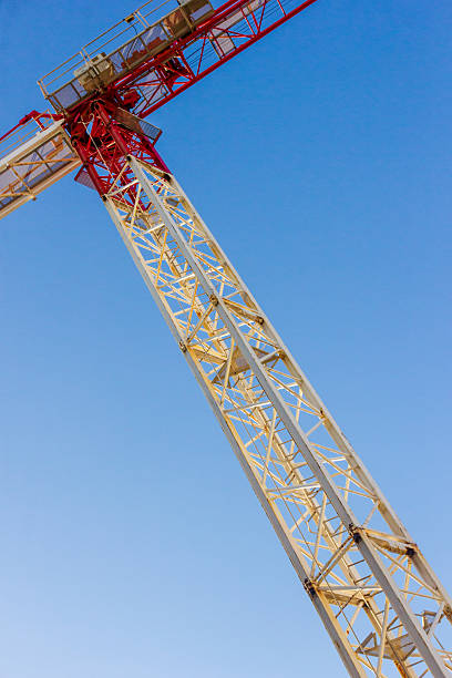 A towering crane painted red and white rises against a vivid blue sky, illustrating industrial construction and engineering in action. Ideal for infrastructure, development, and heavy machinery themes.
