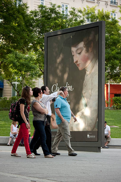 Madrid, Spain - May 13, 2011: Group of adults walking a Madrid street, pausing to view a large outdoor billboard advertising a Chardin art exhibition near the Prado museums, summer urban scene