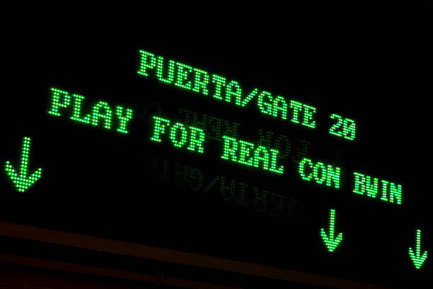 Madrid, Spain - March 16, 2011: Green LED display board at Madrid airport showing Puerta 28 and Play for Real con bwin with down arrows, glowing reflection on dark polished surface—modern travel signage