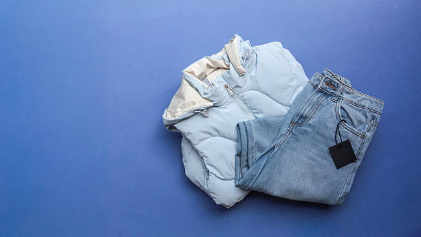 istock Stylish outfit featuring a light blue puffer vest and denim jeans on a blue backdrop. 2238583472